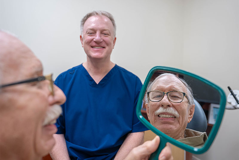 patient looking into mirror after dental implants procedure to see new smile